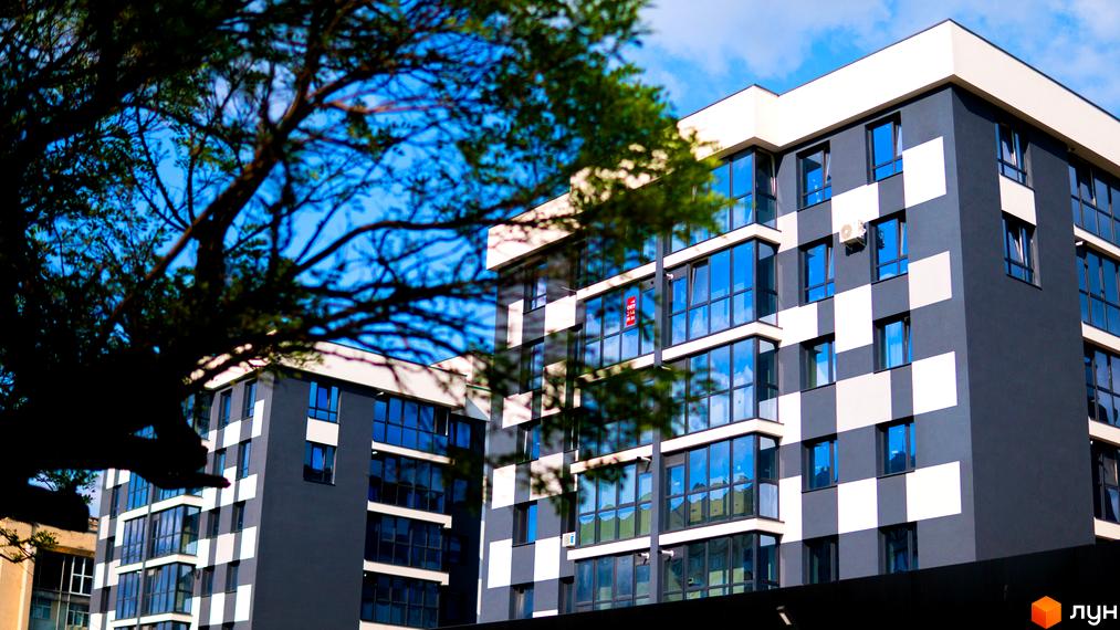 Житловий комплекс Union з темно-сірим та білим фасадом у шаховому порядку та великими скляними вікнами. На передньому плані видно дерево.