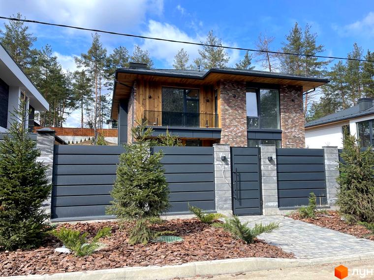 Котеджне містечко КМ Нова Ходосівка Premium. Фасад будинку з цегли та дерева, огороджена територія з парканом та воротами, доріжка з бруківки та зелені.