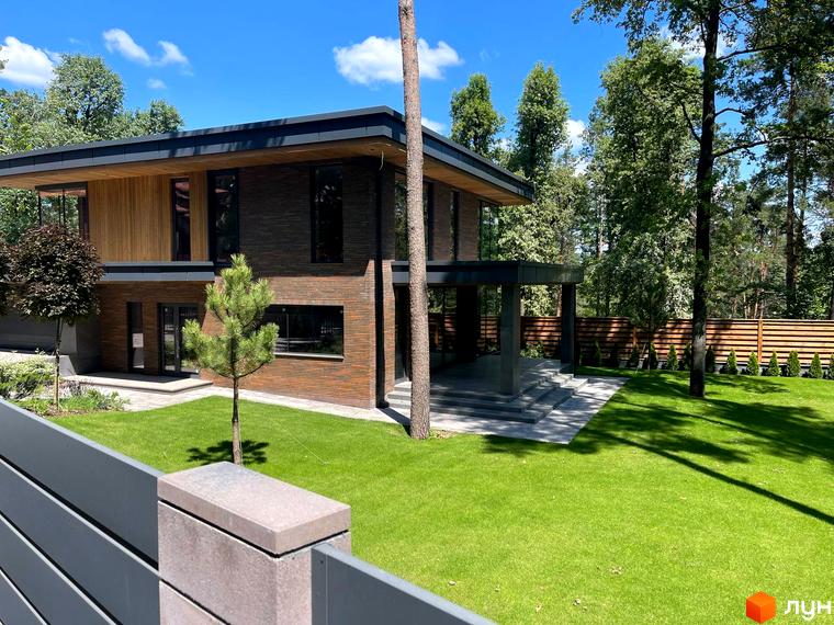 Котеджне містечко Нова Ходосівка Premium. Двоповерховий будинок з дерев'яними та цегляними елементами фасаду, великими вікнами та доглянутим газоном.