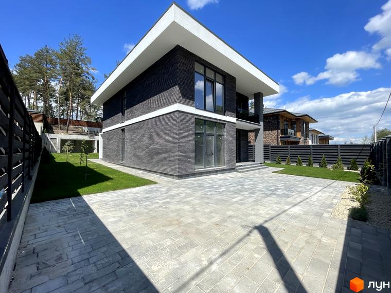 Котеджне містечко КМ Нова Ходосівка Premium. Зовнішній вигляд будинку з темної цегли та великими вікнами, прибудинкова територія з бруківки та зеленої галявини.