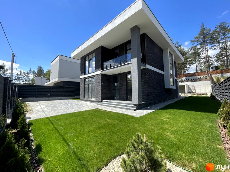 Котеджне містечко Нова Ходосівка Premium. Зовнішній вигляд будинку з темної цегли та прибудинкова територія з зеленим газоном та бруківкою.