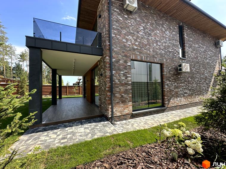 Котеджне містечко Нова Ходосівка Premium. Фасад будинку з цегли, тераса з скляною огорожею та доглянута прибудинкова територія з газоном та доріжками.