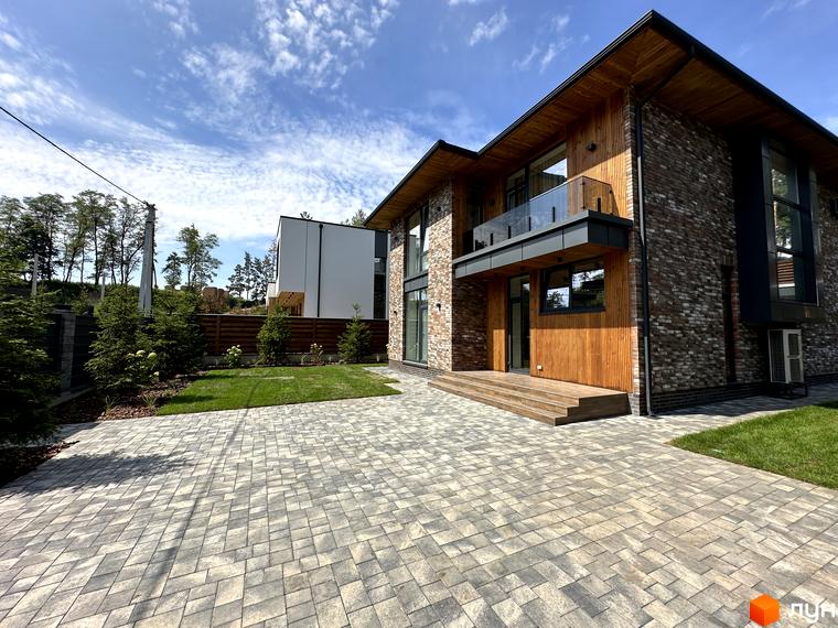 Котеджне містечко КМ Нова Ходосівка Premium: двоповерховий будинок з цегляним та дерев'яним оздобленням, скляним балконом та вимощеною бруківкою прибудинковою територією.