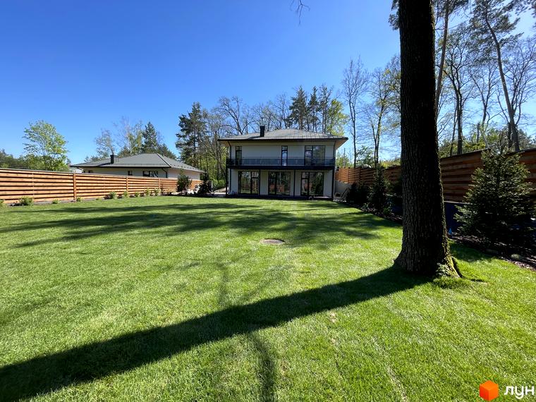 Котеджне містечко Нова Ходосівка Premium. Зовнішній вигляд двоповерхових будинків з великими вікнами та балконами на другому поверсі, доглянутий зелений газон та дерев'яна огорожа.