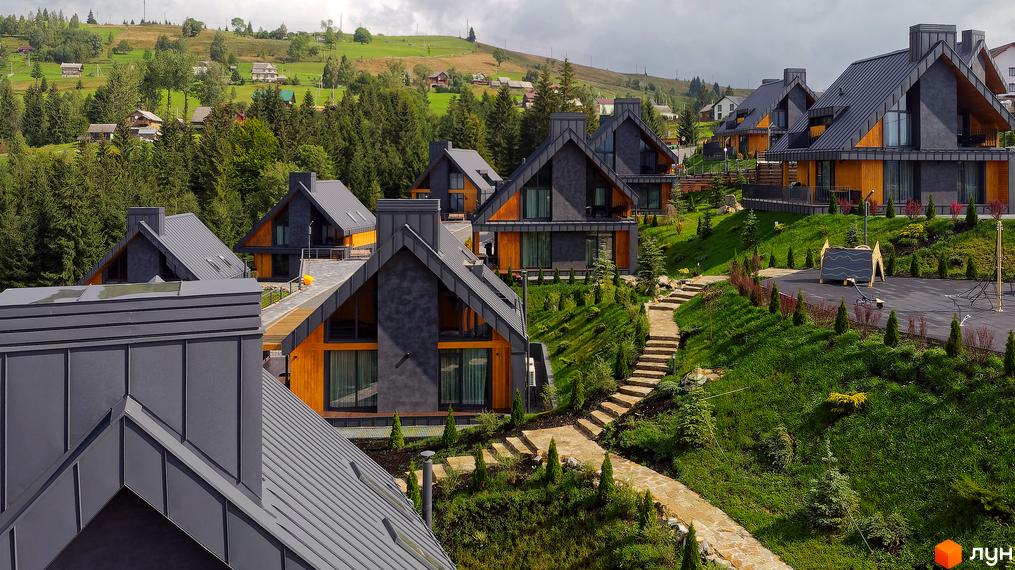 Зображення Котеджного містечка SKOGUR з будинками з сірими дахами та дерев'яним оздобленням. Навколо зелена територія з доріжками.