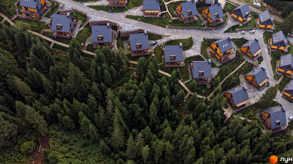 Вигляд зверху на Котеджне містечко SKOGUR з дерев'яними котеджами та темними дахами, розташоване серед зеленого лісу.