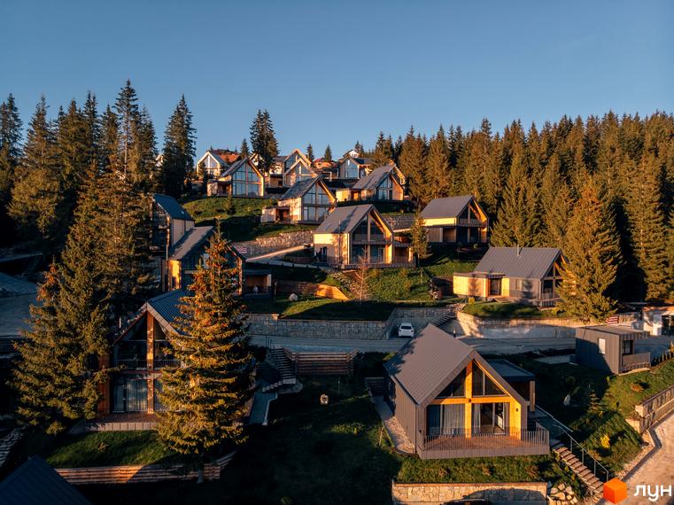 Зображення Котеджного містечка SKOGUR з дерев'яними котеджами на пагорбі серед соснового лісу. Навколо будинків зелені газони.