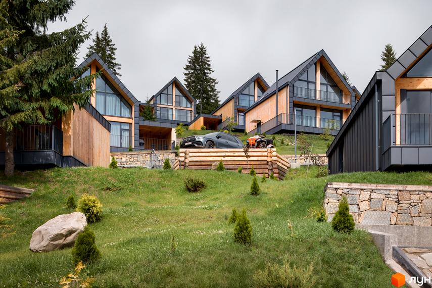 Вигляд на Котеджне містечко SKOGUR з дерев'яними котеджами та великими вікнами на зеленій ділянці.