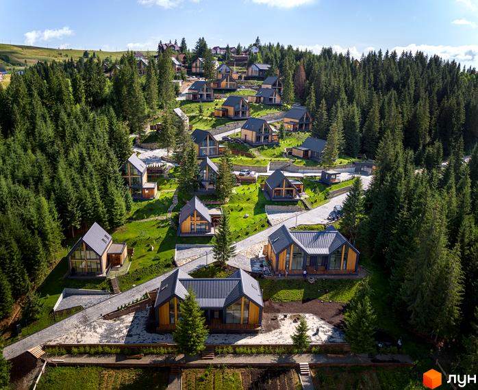 Фото Котеджного містечка SKOGUR з будинками з дерева та великими вікнами. Навколо сосновий ліс та доглянута територія.