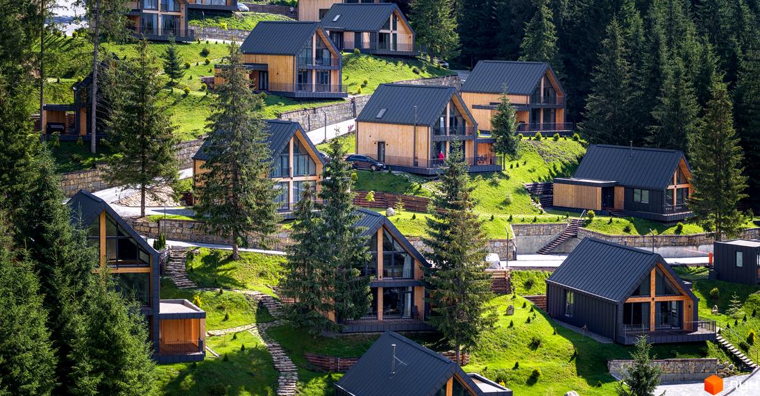 Фото Котеджного містечка SKOGUR з дерев'яними котеджами на зелених пагорбах. Навколо будинків ростуть сосни та облаштовані доріжки.