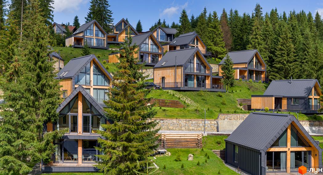 Зображення Котеджного містечка SKOGUR з дерев'яними котеджами на зеленому схилі. Навколо будинків ростуть хвойні дерева.