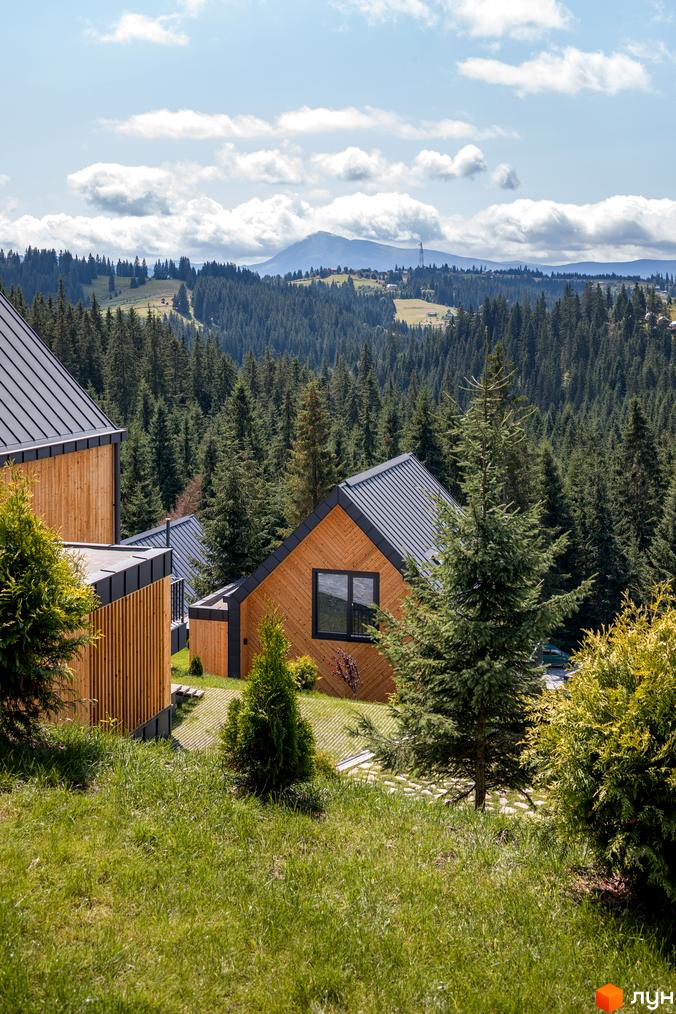 Вигляд котеджів з дерев'яним оздобленням та темним дахом в Котеджному містечку SKOGUR, розташованому серед зелених насаджень та лісів.