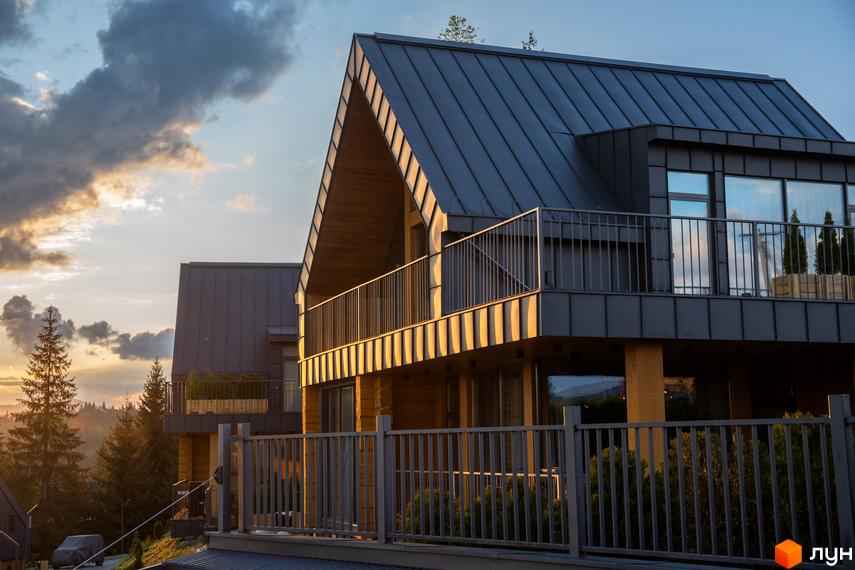 Зображення Котеджного містечка SKOGUR: двоповерхові будинки з темними дахами та дерев'яним оздобленням, огороджені металевими парканами.