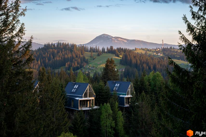 Котеджне містечко SKOGUR серед хвойного лісу. Два будинки з темними дахами на пагорбі з видом на гори.