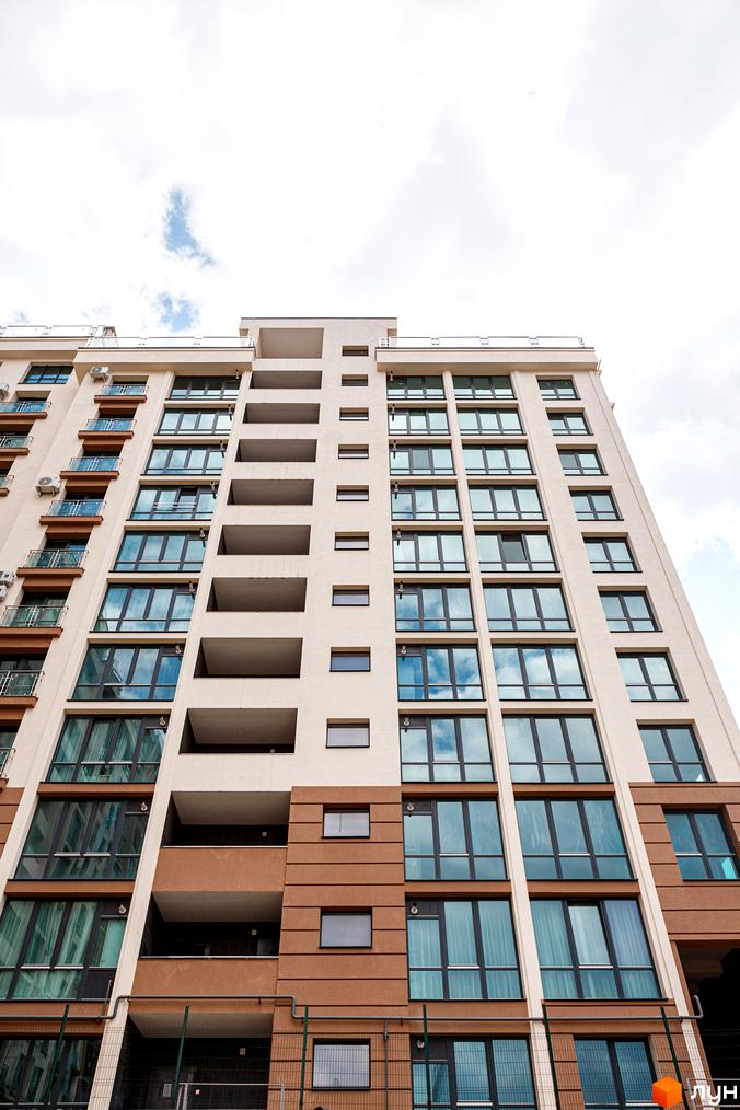 Фасад Житлового комплексу HydroPark DeLuxe: висока будівля з бежевими та коричневими секціями, великими вікнами та балконами.