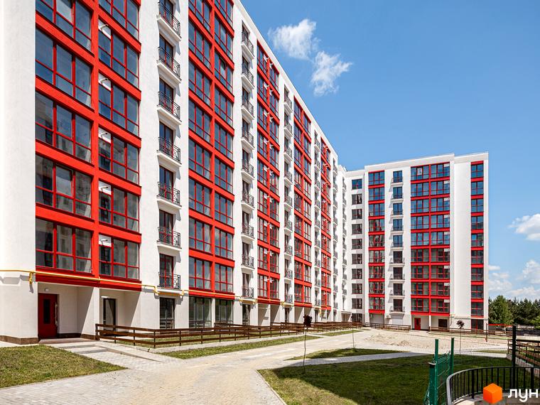 Житловий комплекс Містечко Козацьке: багатоповерхові будинки з білими фасадами та червоними віконними рамами. Прибудинкова територія має доріжки та зелені газони.