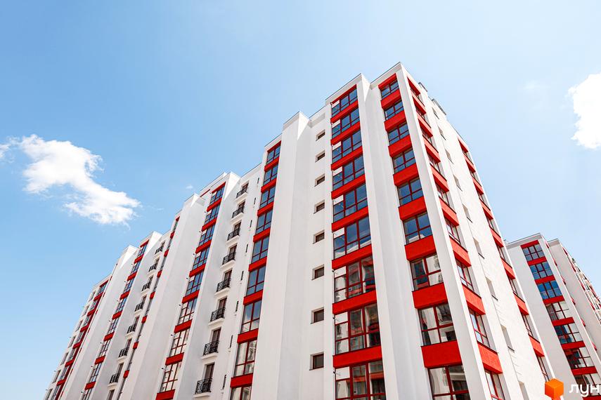 Фасади багатоповерхових будинків Житлового комплексу Містечко Козацьке білого кольору з червоними вікнами та балконами, на тлі ясного неба.