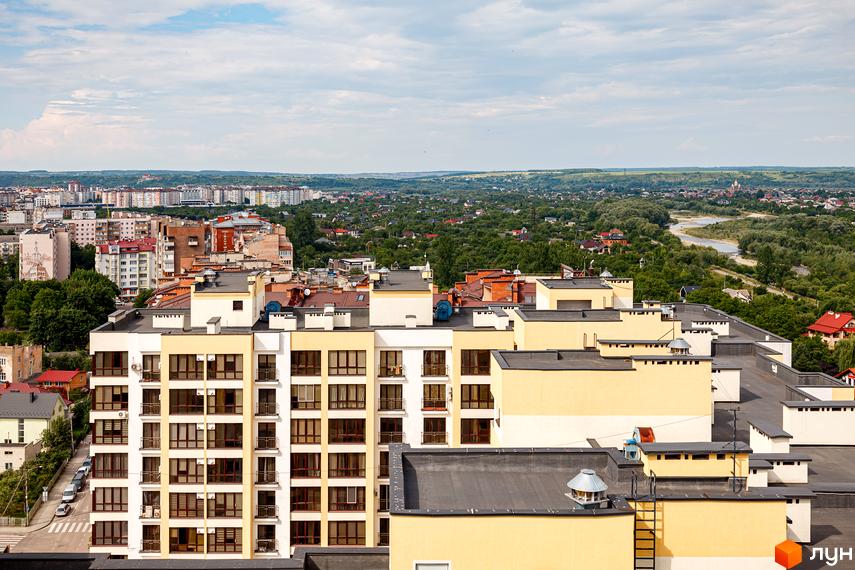 Вигляд фасаду житлового комплексу Lystopad з вікнами та балконами. Навколо розташовані інші будівлі та зелені насадження.