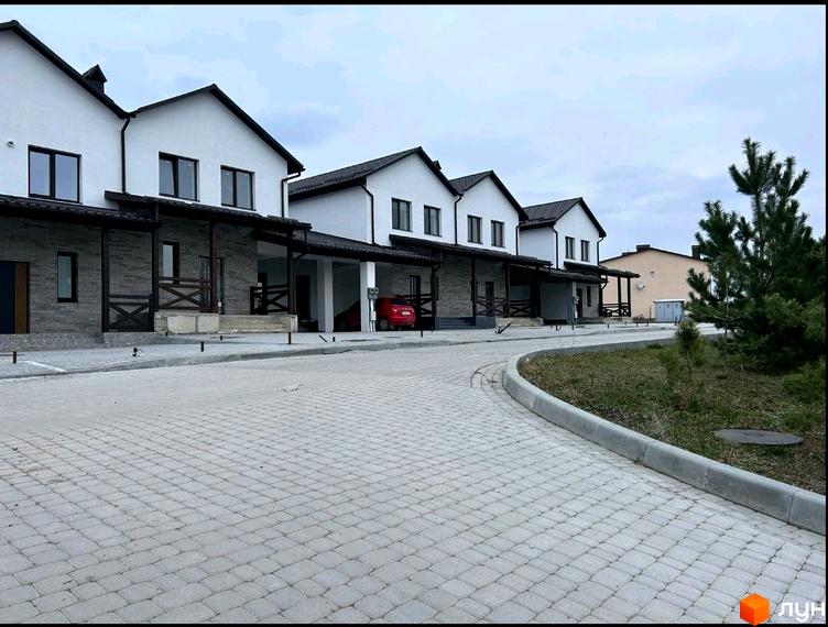 Котеджне містечко КМ Затишний: фасади будинків з білою штукатуркою та темними дахами, вимощена бруківкою прибудинкова територія з деревами.