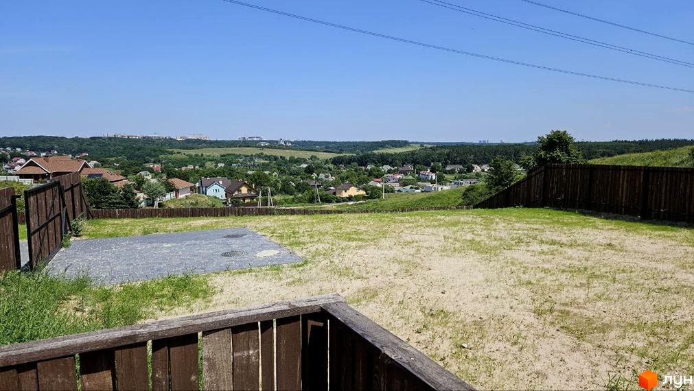 Вид на котеджне містечко KRAIEVYD з панорамним краєвидом на зелені пагорби та міську забудову. На передньому плані - ділянка з бруківкою та дерев'яним парканом.