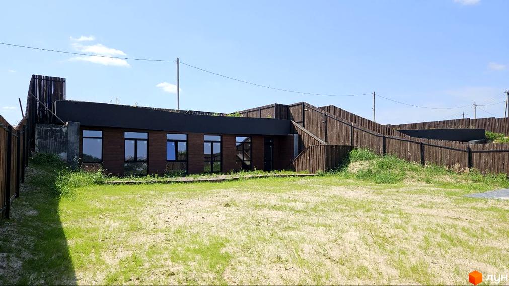 Котеджне містечко KRAIEVYD: двоповерхова будівля з коричневим фасадом та великими вікнами, оточена дерев'яним парканом та зеленою ділянкою.