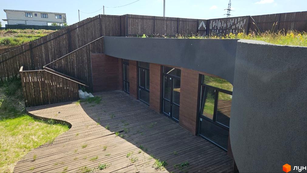 Зовнішній вигляд комплексу KRAIEVYD з дерев'яним оздобленням та великими вікнами. Прибудинкова територія з дерев'яною терасою та зеленими насадженнями.