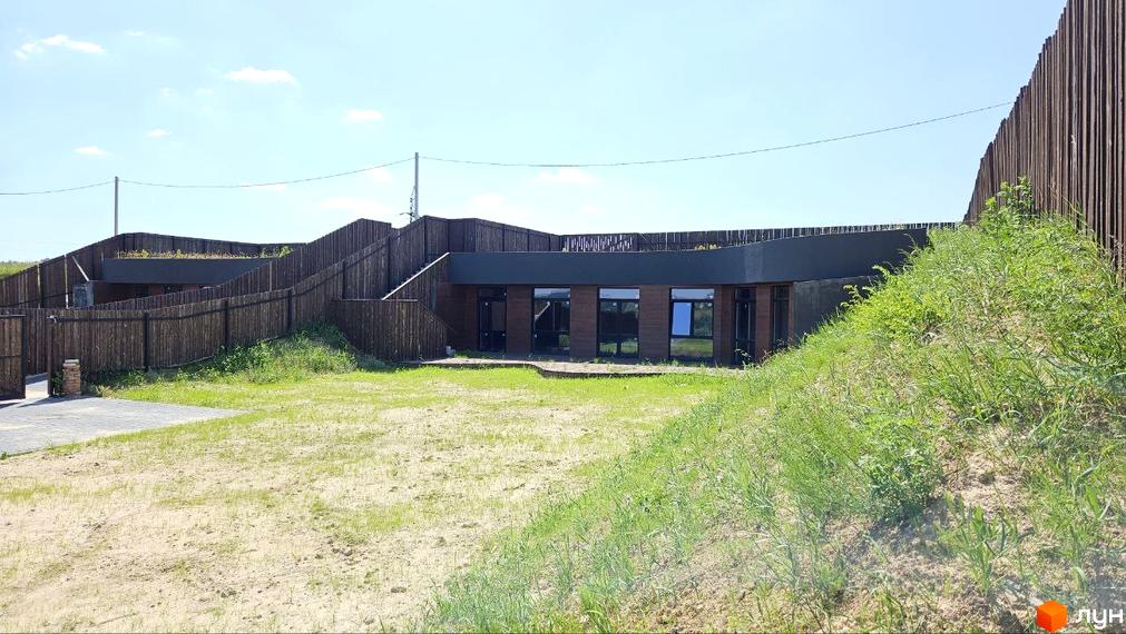 Котеджне містечко KRAIEVYD: сучасна новобудова з дерев'яним фасадом та великими вікнами, оточена зеленим ландшафтом та дерев'яним парканом.