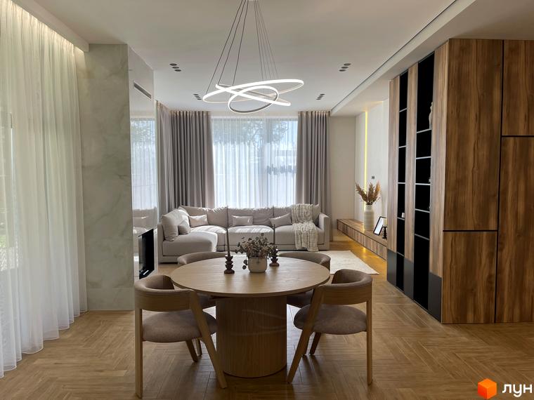 Інтер'єр Котеджного містечка Нова Ходосівка з обіднім столом та диваном. Світла кімната з великими вікнами та паркетною підлогою.