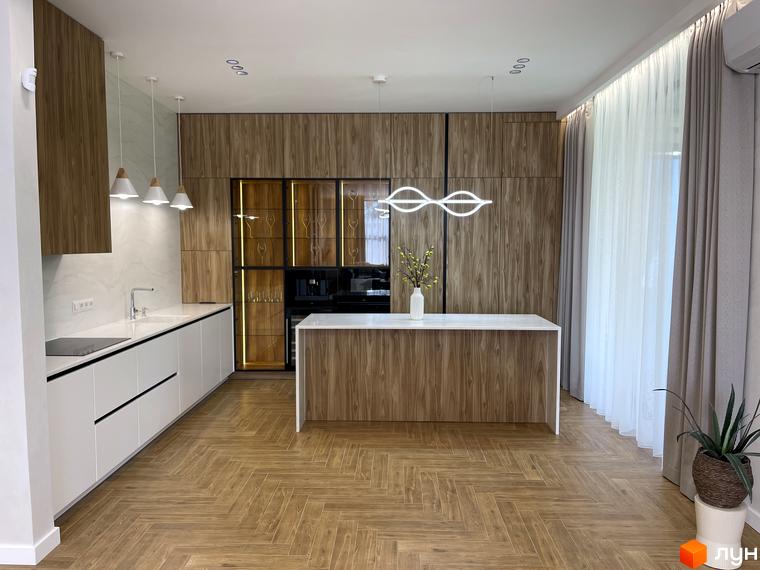 Простора кухня в Котеджному містечку Нова Ходосівка з дерев'яними шафами, білими стільницями та підлогою ялинкою. Інтер'єр доповнюють підвісні світильники.