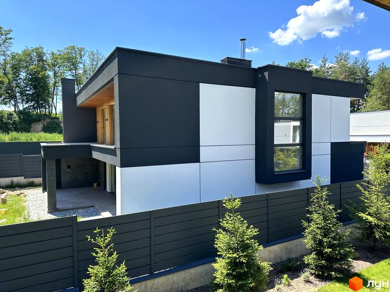 Вигляд двоповерхового будинку в Котеджному містечку Нова Ходосівка з великими вікнами та сірим парканом. Навколо будинку зелені насадження.