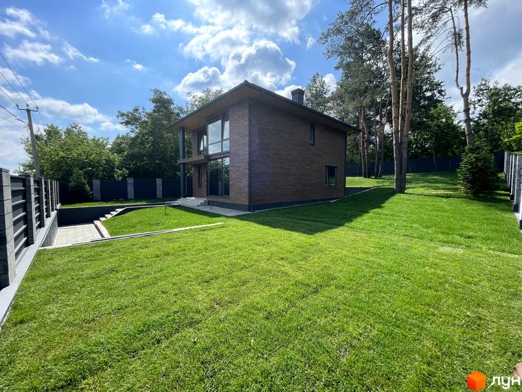 Котеджне містечко Нова Ходосівка: двоповерховий будинок з великими вікнами та темним фасадом, навколо зелений газон та сосни.