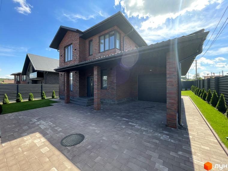 Зображення двоповерхового цегляного будинку в Котеджному містечку Нова Ходосівка. Навколо будинку вимощена бруківка та висаджені декоративні туї.