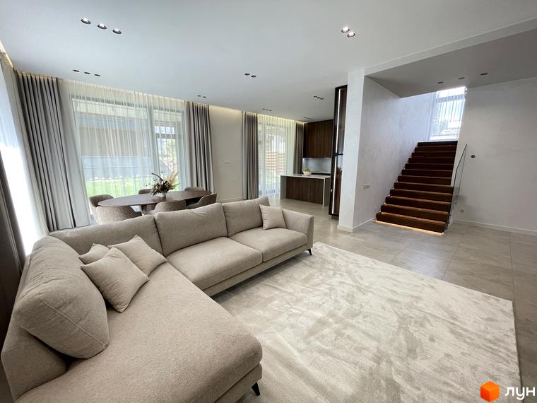 Інтер'єр вітальні в Котеджному містечку Нова Ходосівка: диван, сходи на другий поверх та велике вікно з видом на зелений газон.