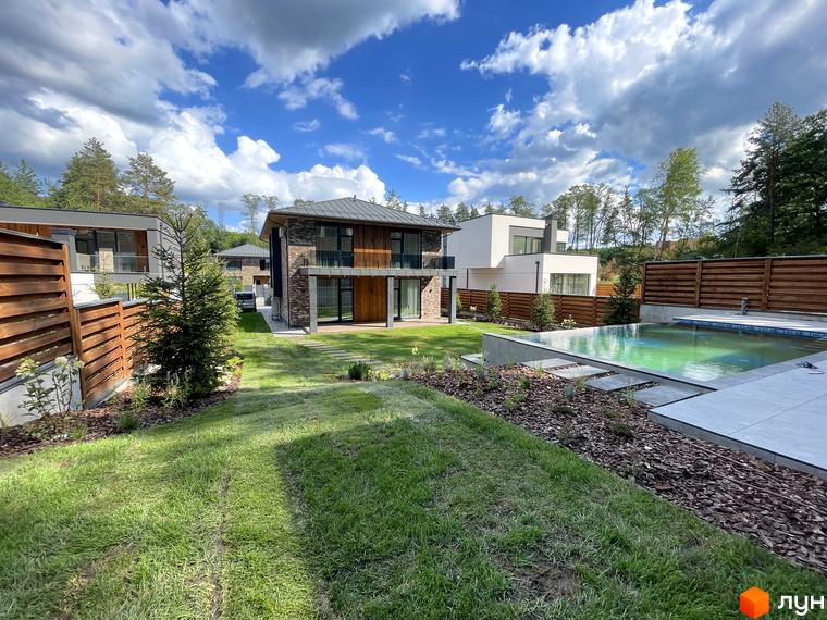 Зображення будинку з великими вікнами та терасою в Котеджному містечку Нова Ходосівка. Навколо зелений газон та басейн.