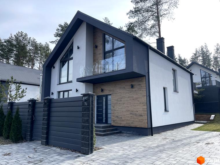 Фасад білого будинку з темно-сірим дахом, великими вікнами та дерев'яними елементами. Територія Котеджного містечка Нова Ходосівка з бруківкою та парканом.