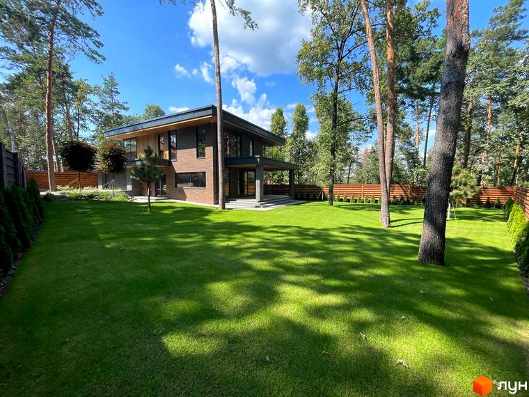 Вигляд двоповерхового будинку з великими вікнами в Котеджному містечку Нова Ходосівка. Навколо будинку зелений газон та дерева.