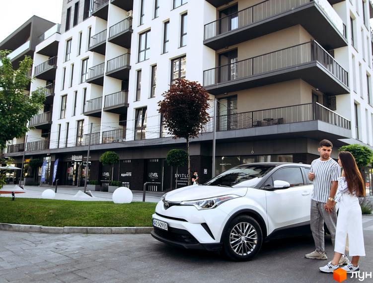 Висотна будівля ЖК Sky Towers з балконами та панорамними вікнами. На передньому плані доглянута прибудинкова територія з газоном та білим автомобілем.