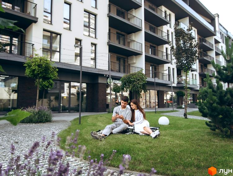 Зовнішній вигляд багатоповерхового будинку ЖК Sky Towers з балконами та великими вікнами. На газоні перед будинком відпочиває пара.