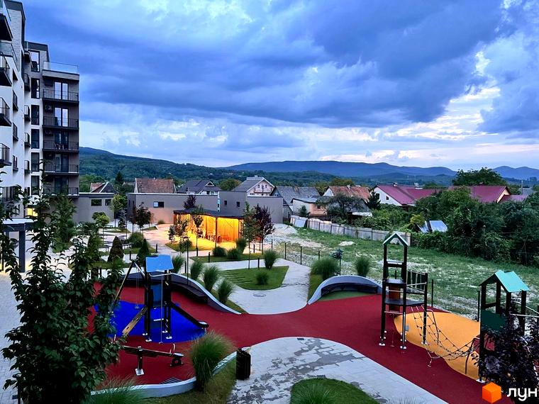 Вигляд житлового комплексу Sky Towers з дитячим майданчиком та будівлями на фоні гір. Простора прибудинкова територія з ландшафтним дизайном.