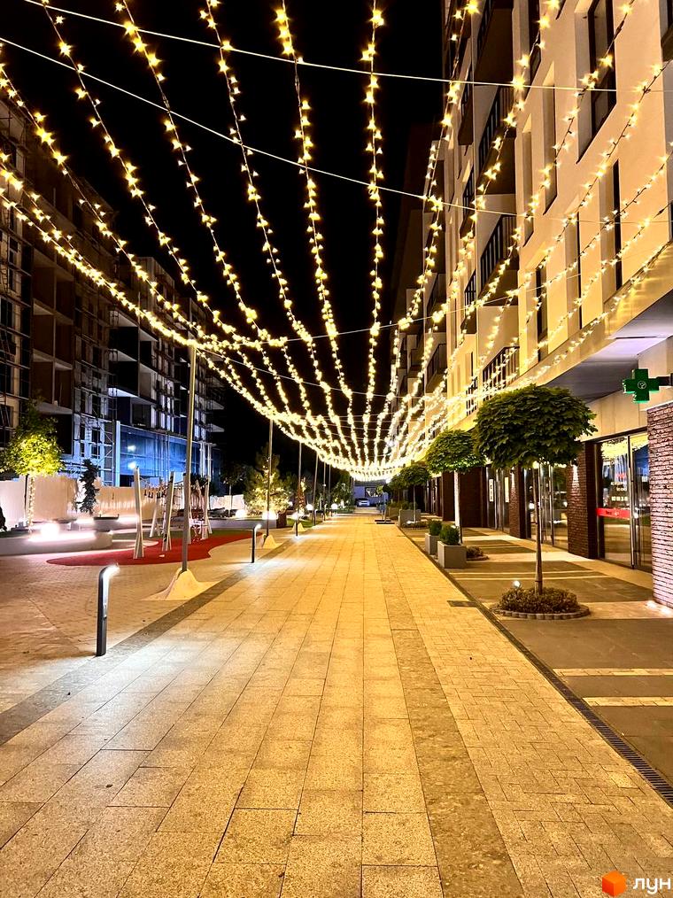 Житловий комплекс Sky Towers з вуличною ілюмінацією та доглянутою прибудинковою територією, що створює затишну атмосферу ввечері.