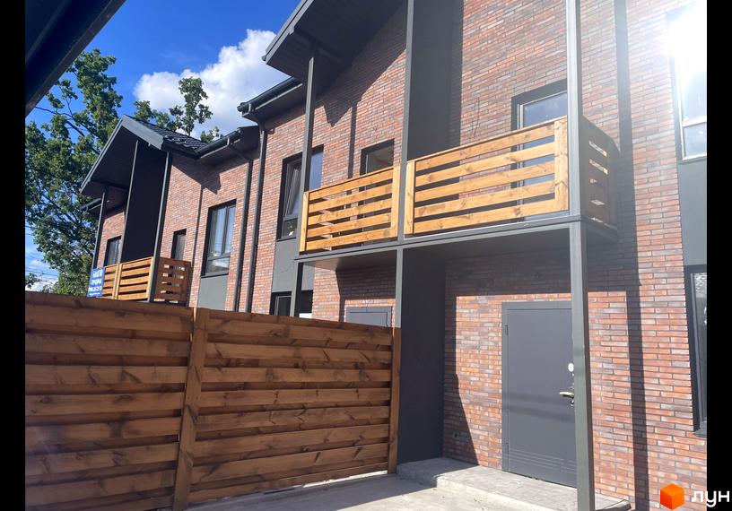 Таунхауси „Сингаївського“: двоповерхові будинки з червоної цегли з дерев'яними балконами та парканом.