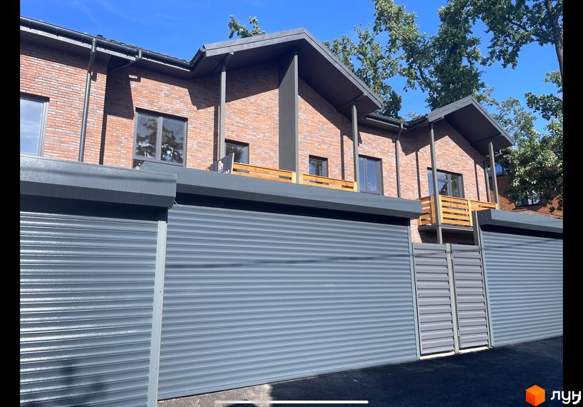 Таунхауси Сингаївського: цегляні фасади, панорамні вікна та ролетні гаражні ворота. Прибудинкова територія з доглянутим ландшафтом.