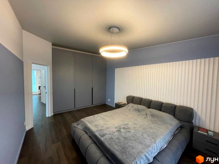 Спальня в КМ Sunrise Residence з великим ліжком та приліжковими тумбами. Сірі шафи та світла стіна за ліжком створюють затишок.