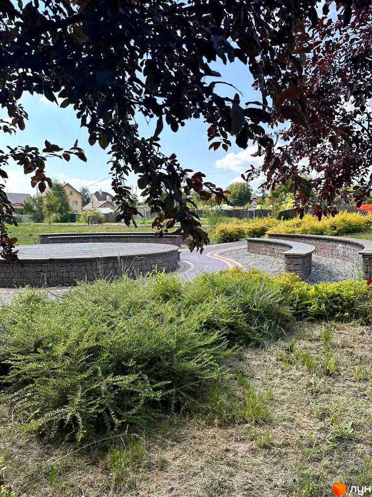 Житловий комплекс Riviera: оглядовий майданчик з кам'яними стінами та зеленою зоною. Територія навколо новобудови з доріжками та кущами.