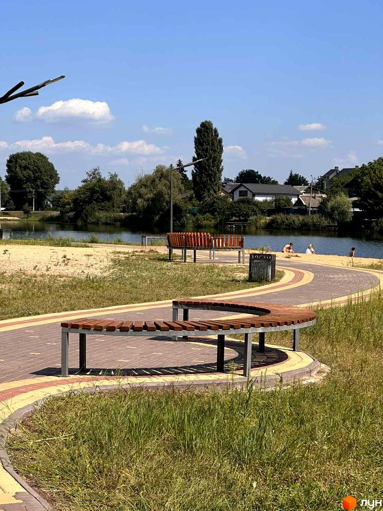 Житловий комплекс Riviera з зоною відпочинку біля озера. Набережна з лавками та піщаним пляжем для відпочинку.