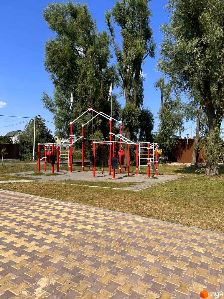 Спортивний майданчик з турніками та боксерськими грушами біля ЖК Riviera. Зелена територія та бруківка навколо.