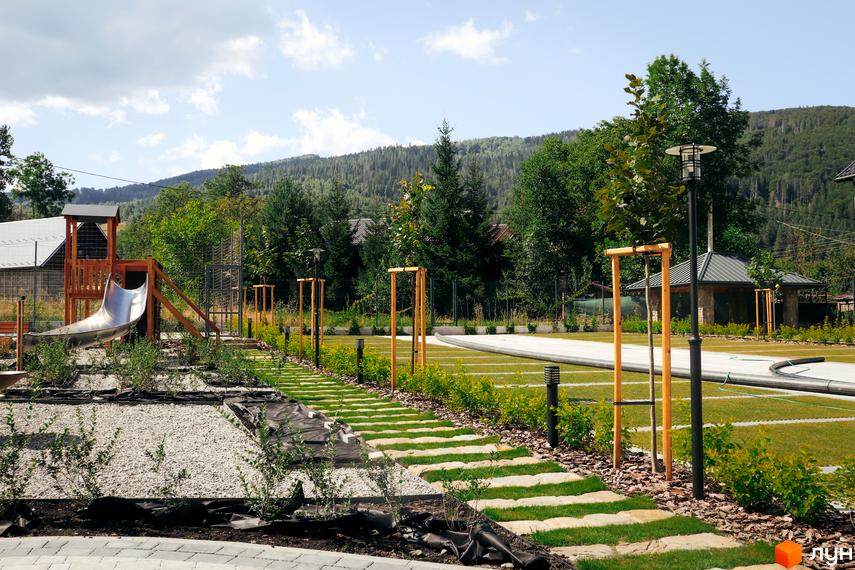 Дитячий майданчик та доглянута прибудинкова територія ЖК Крайобраз з елементами ландшафтного дизайну. Зелені насадження та доріжки створюють затишну атмосферу для відпочинку.