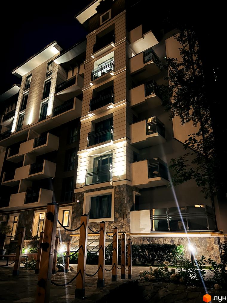 Житловий комплекс Крайобраз. Нічне фото фасаду будинку з балконами та підсвічуванням. Прибудинкова територія з деревами та освітленням.