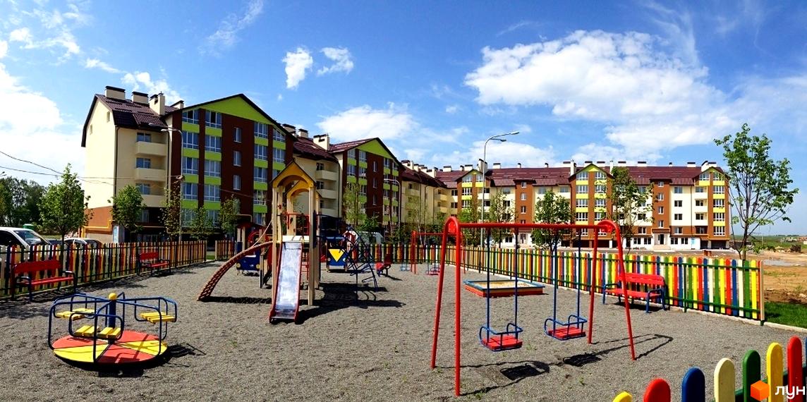 Житловий комплекс Львівський маєток з яскравим дитячим майданчиком та кольоровим парканом. Новобудова має коричнево-зелену фасадну обробку та коричневий дах.