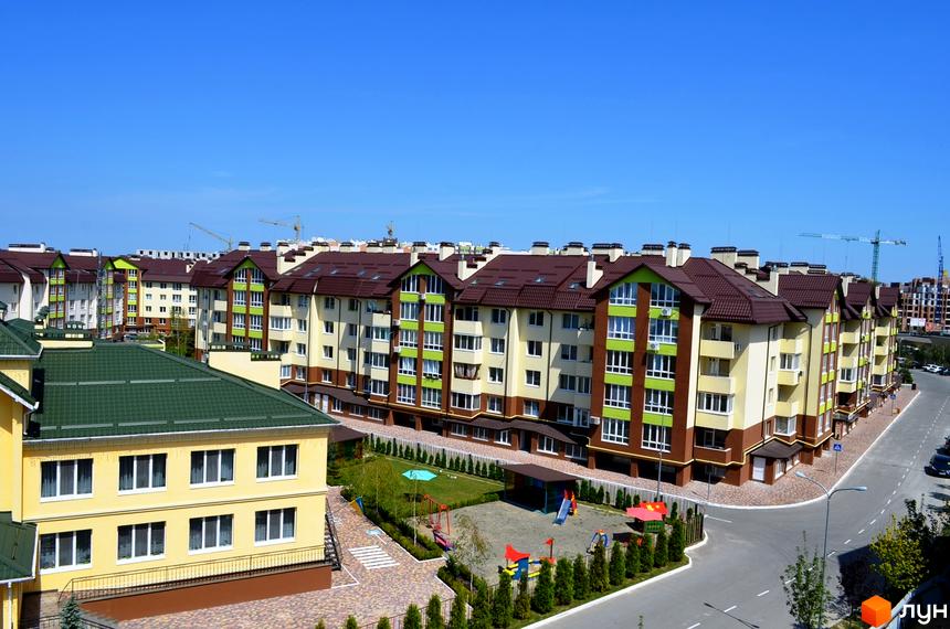 Житловий комплекс Львівський маєток: багатоповерхові будинки з коричневими дахами та світлими фасадами з зеленими акцентами. Поруч дитячий майданчик та зелена зона.